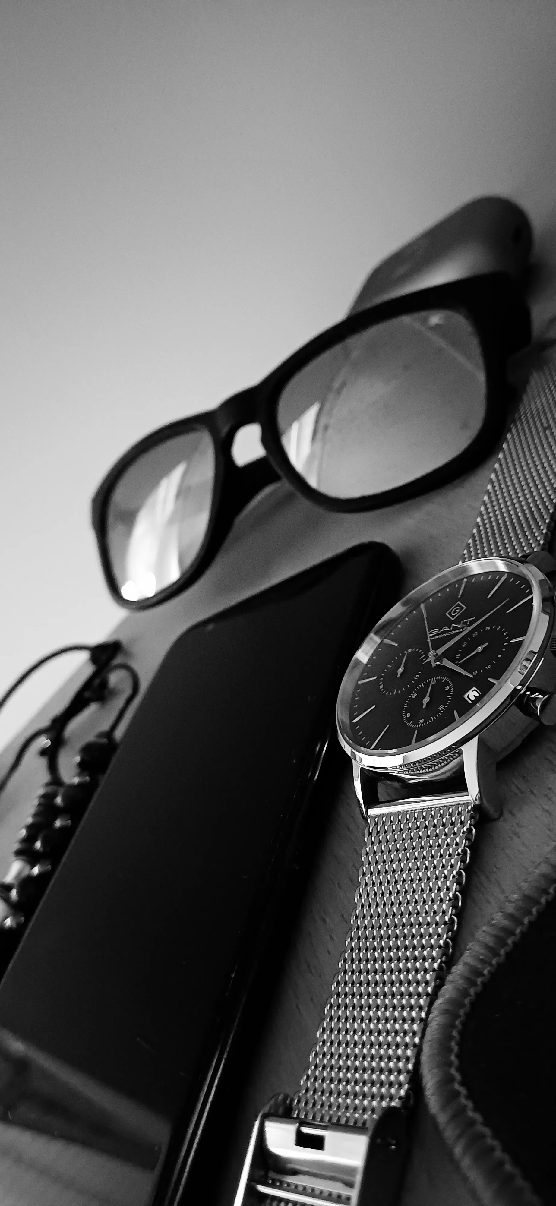Picture of a watch, a phone and glasses on a table.